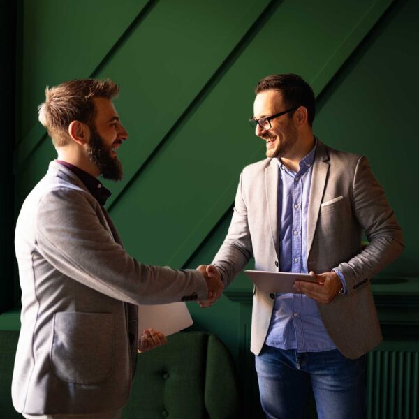 Two business professionals shaking hands after a successful meeting while holding contracts and a tablet.