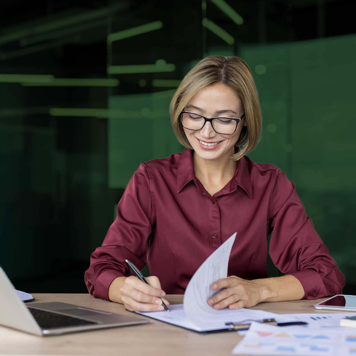 Professional reviewing and signing business documents at a desk with a laptop and paperwork.